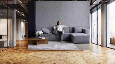 Portrait of happy woman feeling lazy, stretching on sofa and smiling pleased, relaxing at home, resting from work. Wall mural